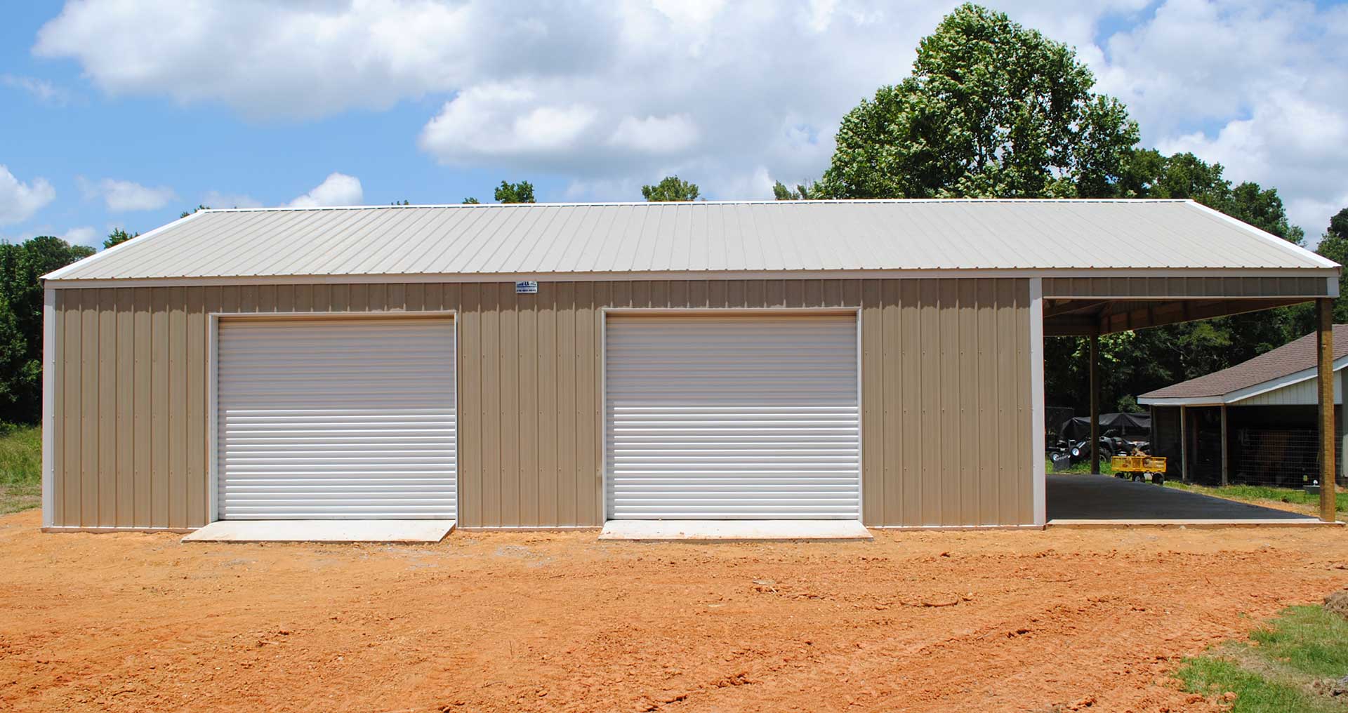 Two-car beige garage with white roll-up doors on a dirt lot under a cloudy sky