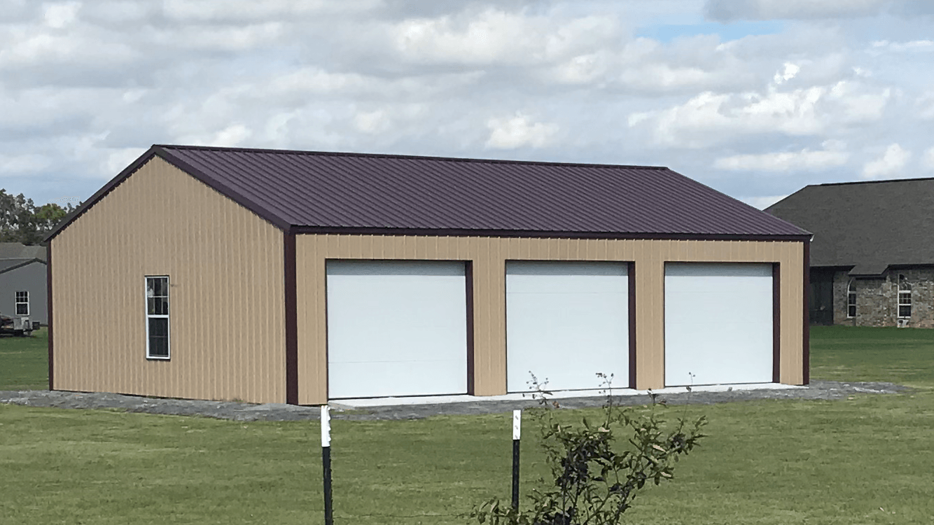 Tan metal garage with three white roll-up doors on a grassy lot