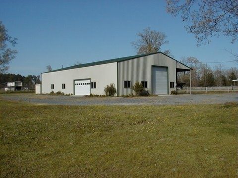 Small white industrial building with a garage door and black trim in a grassy lot under a blue sky