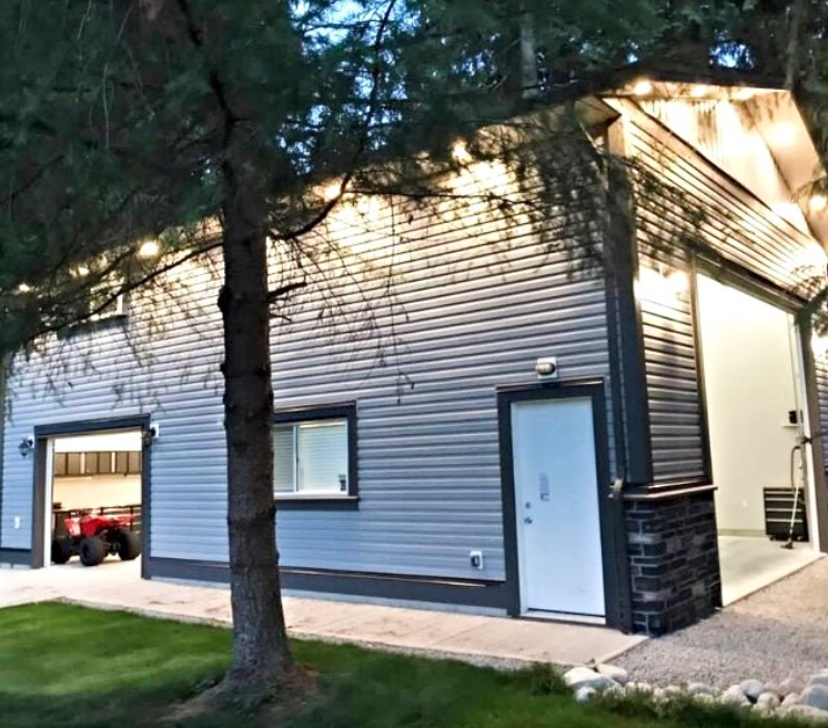 White-sided garage and side entrance of a house at dusk, with a tree and lawn in the foreground