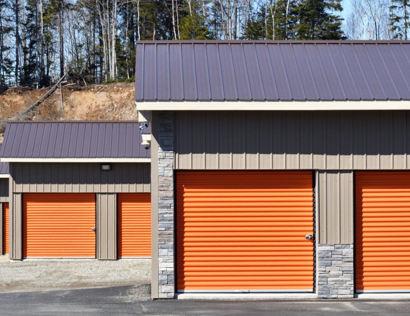Row of orange storage unit doors with dark metal roofs and trees in the background