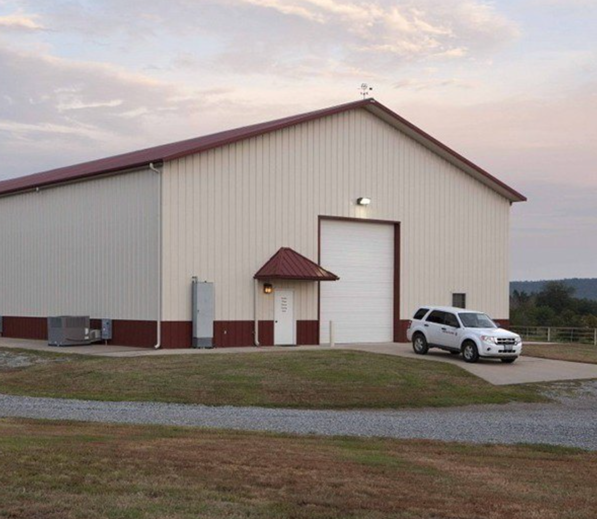 Large beige warehouse with red trim, a side entrance, and a white SUV parked outside at dusk.