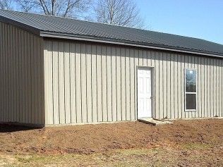 Metal-sided building with a white door and window on a bare dirt lot.