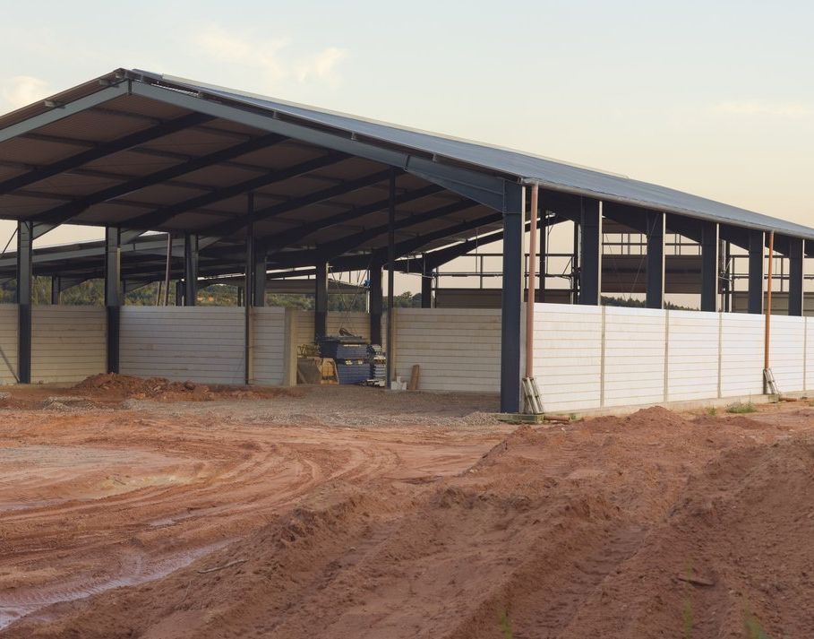 Open-sided metal barn on a dirt lot, with a red-brown roof and white walls.