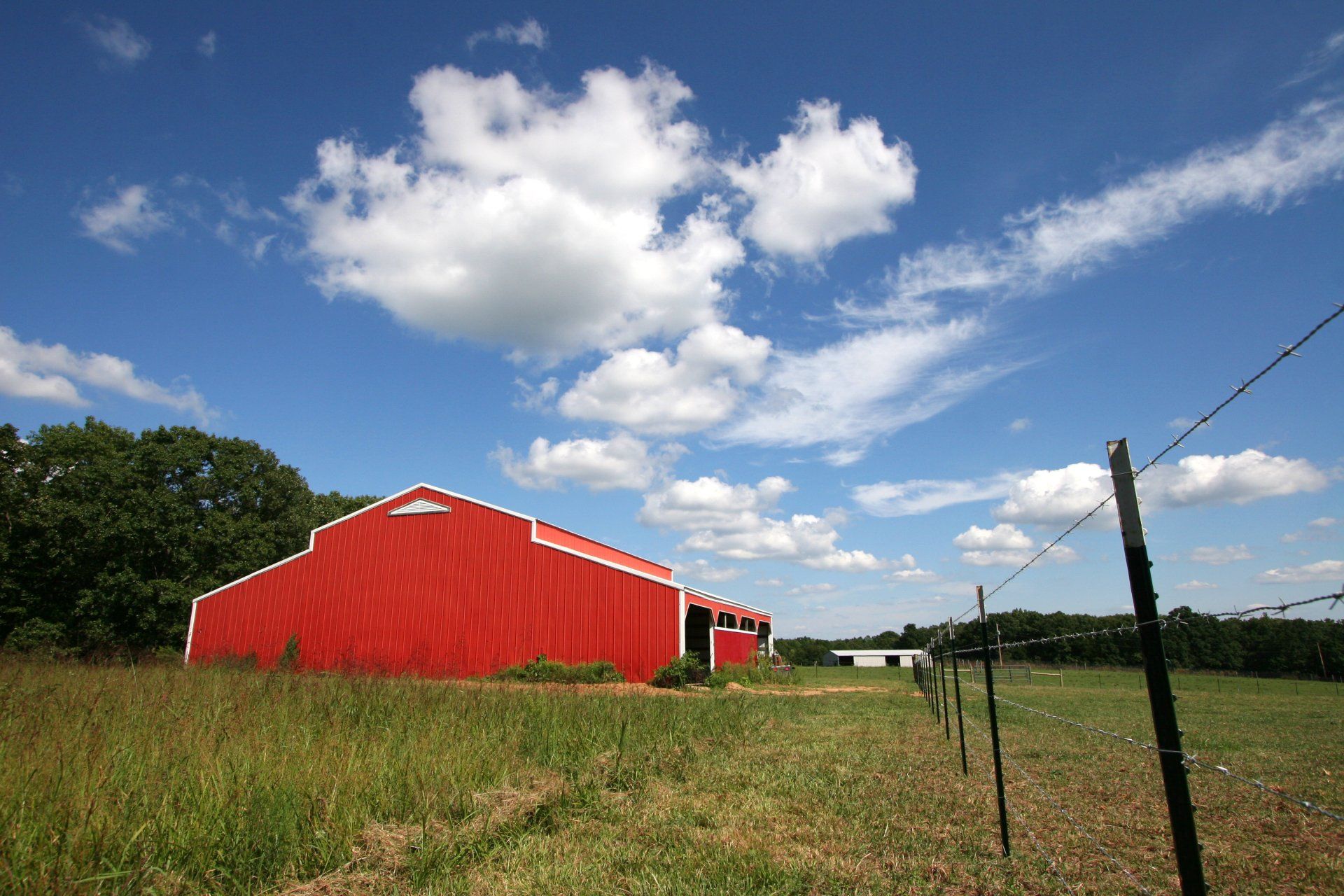 Red barn in a grassy field under a bright blue sky with scattered clouds