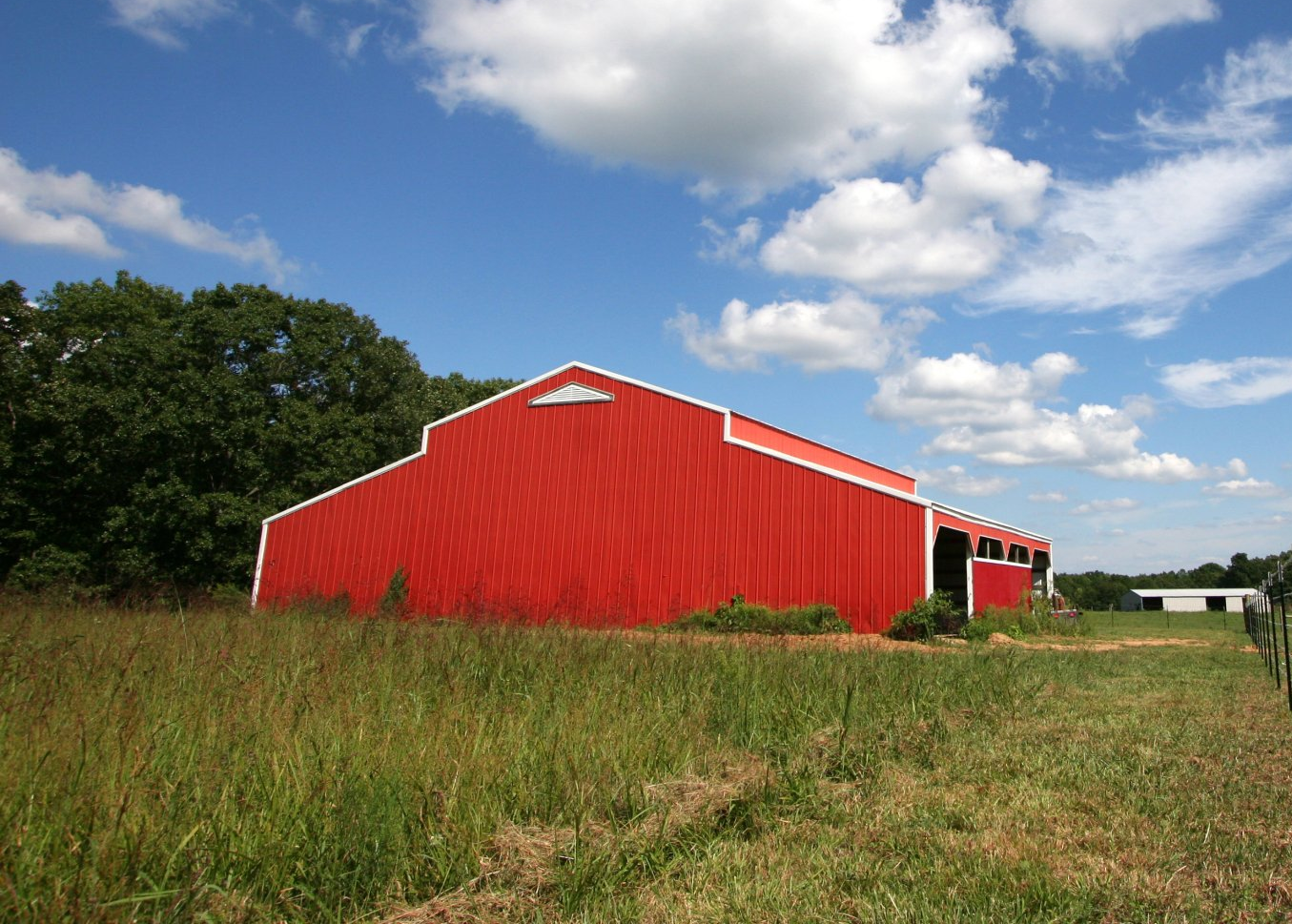 Red barn in a grassy field under a blue sky with clouds
