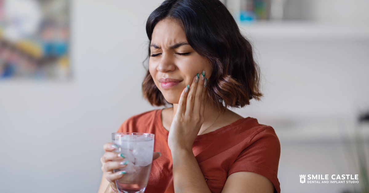 Woman holding a glass of water and pressing her cheek, wincing in pain in a home setting