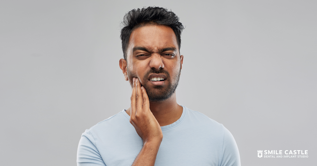 Man grimacing and holding his cheek against tooth pain on a gray background