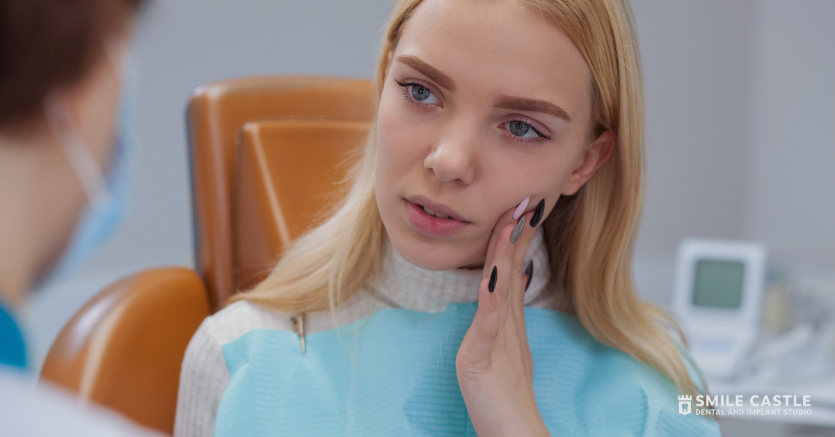 Woman in a light blue top resting her hand on her cheek, listening thoughtfully in a clinic office.