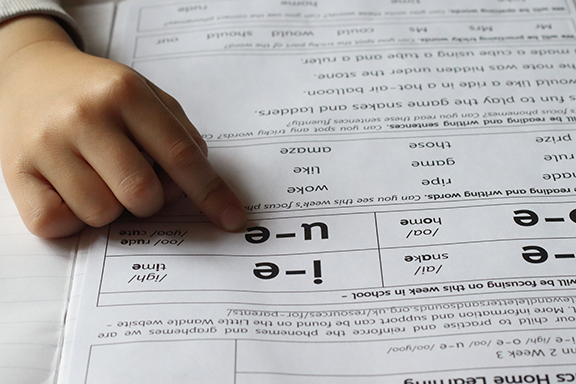 A child's hand pointing at a word list on a worksheet; phonics activity.