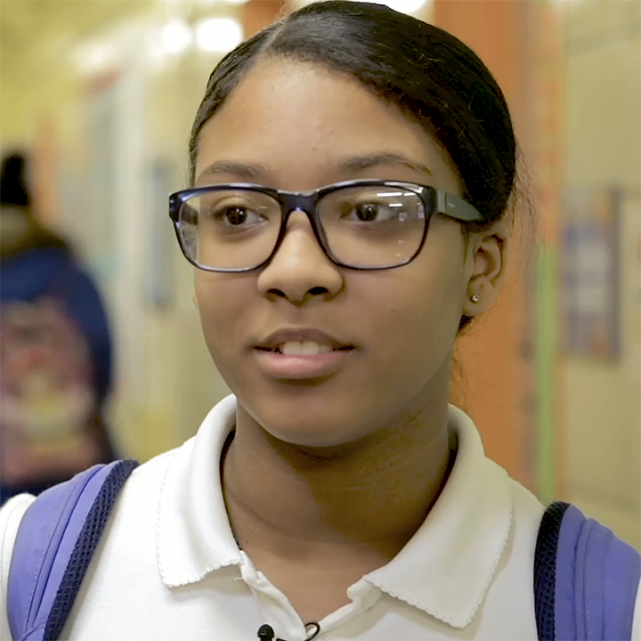Teenager with glasses, a school backpack, stands in a hallway and talks.