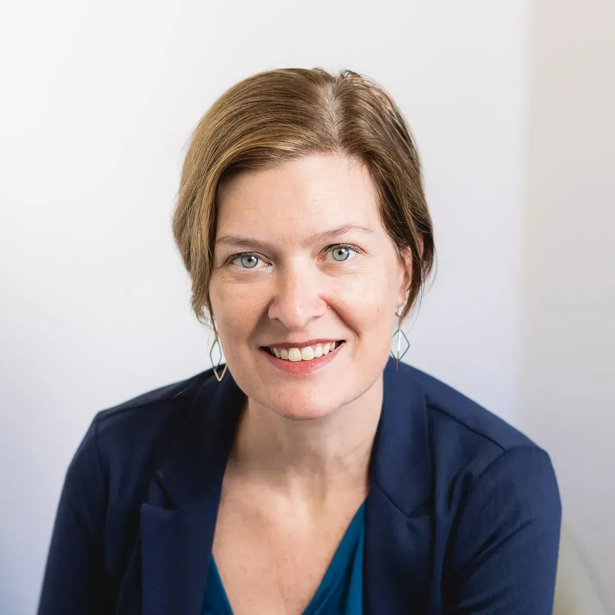 Woman with fair skin and short brown hair, wearing a blue blazer and smiling.