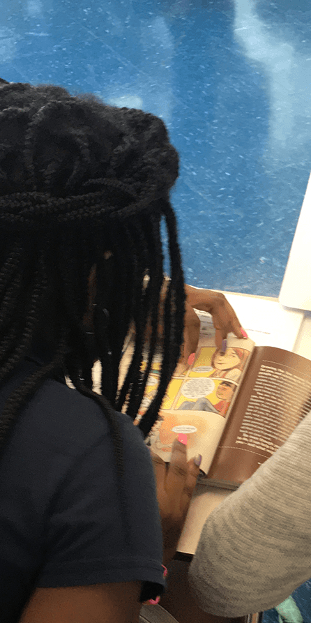 Person with long, dark braids reads a book with illustrations.