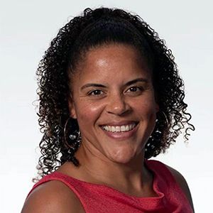 Woman with curly dark hair smiles, wearing a red top and hoop earrings.