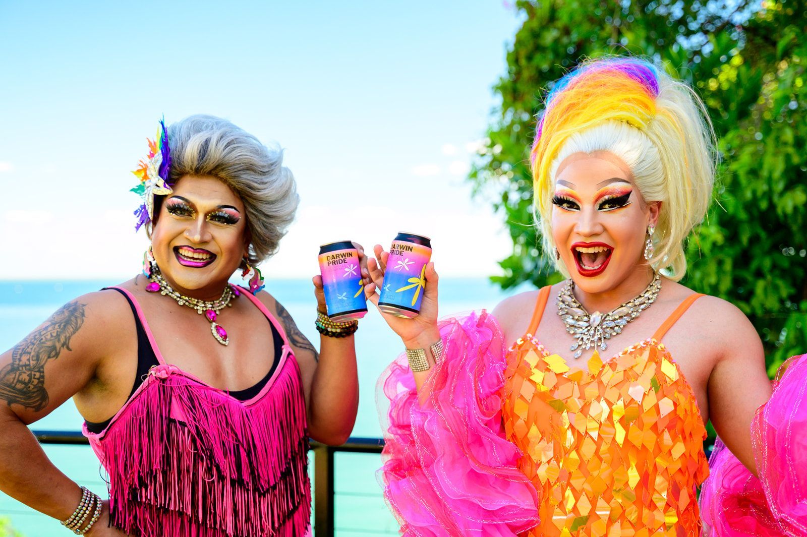 Two drag queens are standing next to each other on a balcony holding drinks.