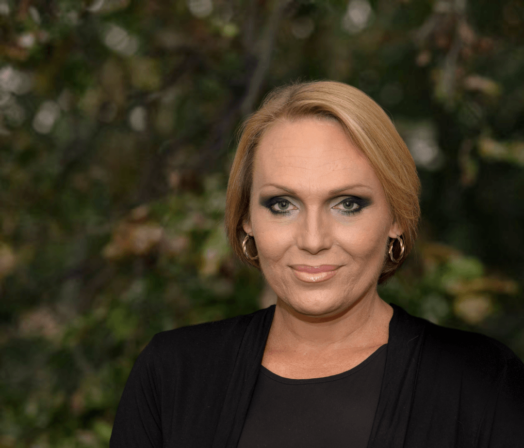 A woman wearing a black jacket and earrings is smiling for the camera.