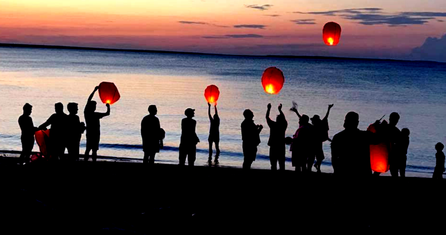 A group of people holding lanterns on the beach at sunset