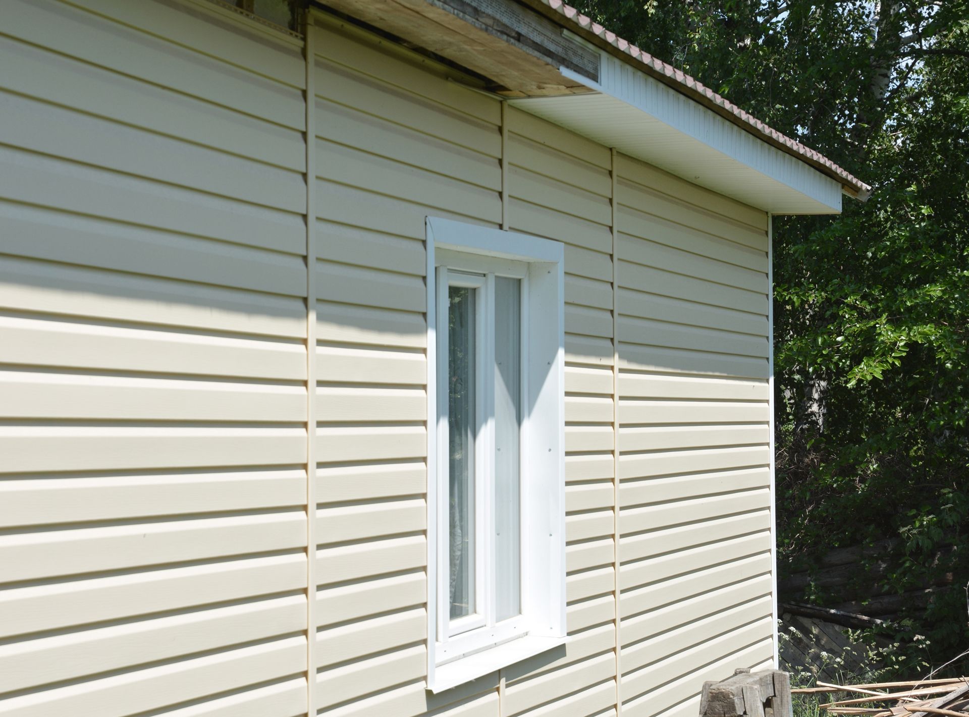 Beige vinyl siding on a building with a white window and a portion of a roof.