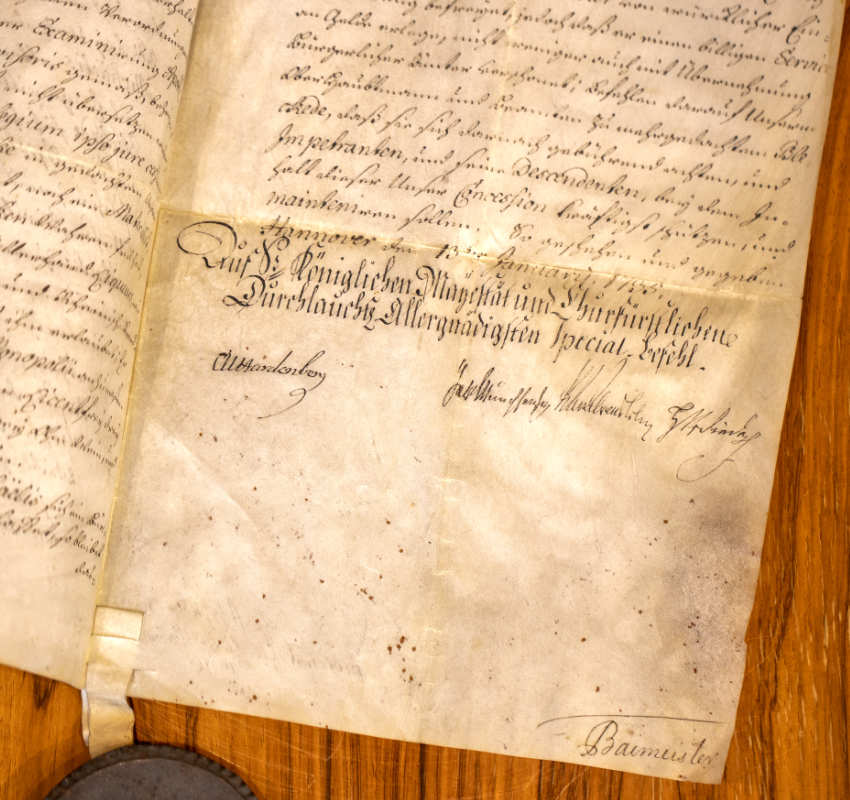 Ein altes, vergilbtes Dokument mit handgeschriebener deutscher Kurrentschrift, auf einer Holzoberfläche platziert, mit amtlichen Unterschriften.