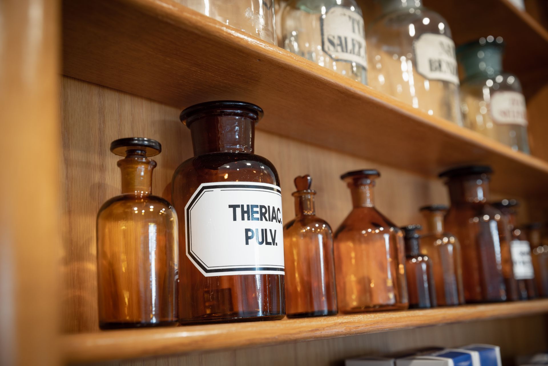 Bernsteinfarbene Apothekerflaschen mit Etiketten auf Holzregalen in einer altmodischen Apotheke.