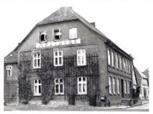 Ein Schwarzweißfoto eines mehrstöckigen Backsteingebäudes mit dem Wort „APOTHEKE“ an der Fassade.