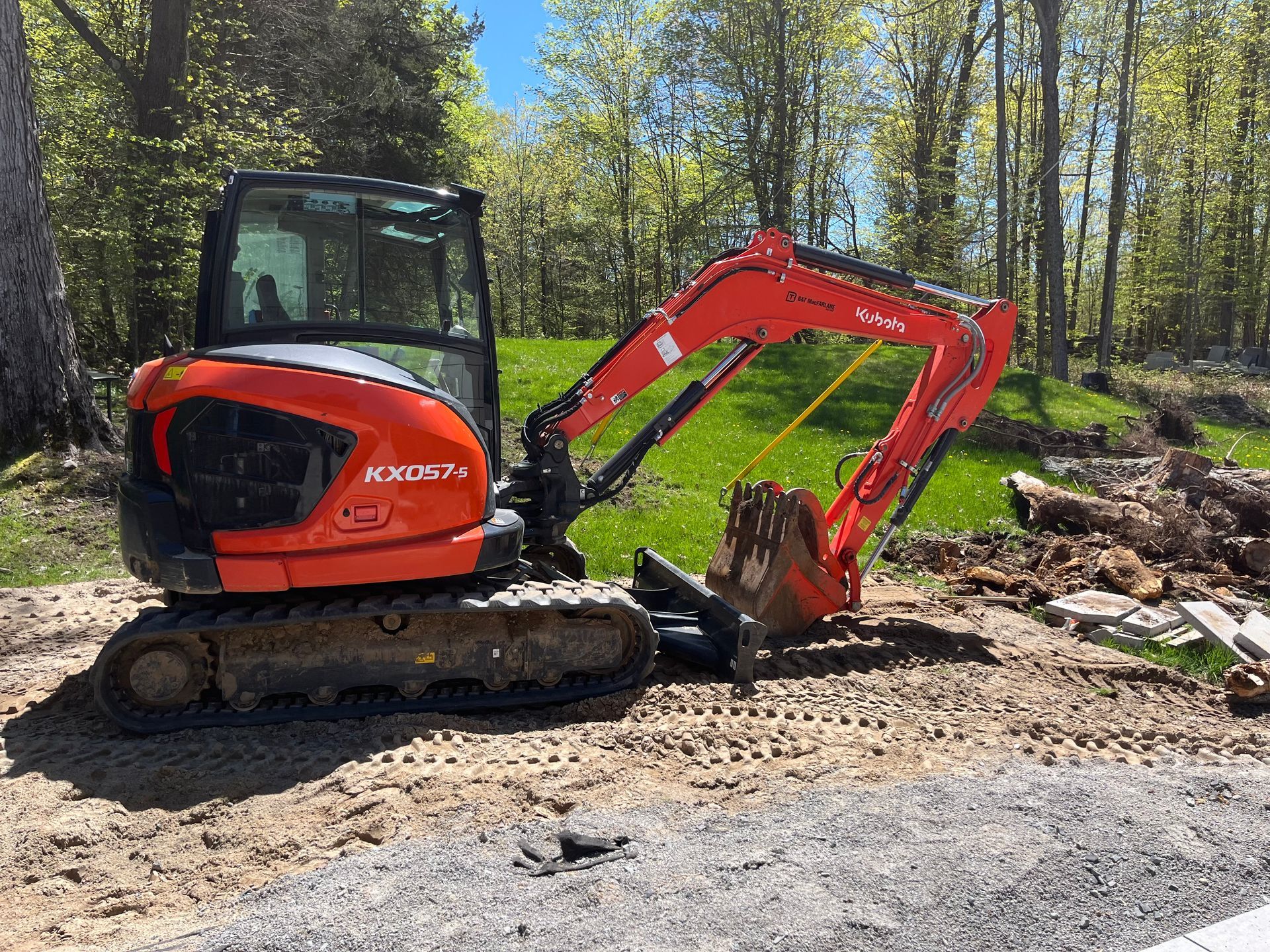 Orange Kubota mini excavator on gravel, with arm extended, in a grassy outdoor setting.