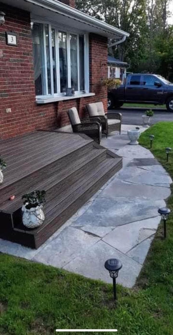 Brick house with wooden deck, stone path, chairs, and garden lights.