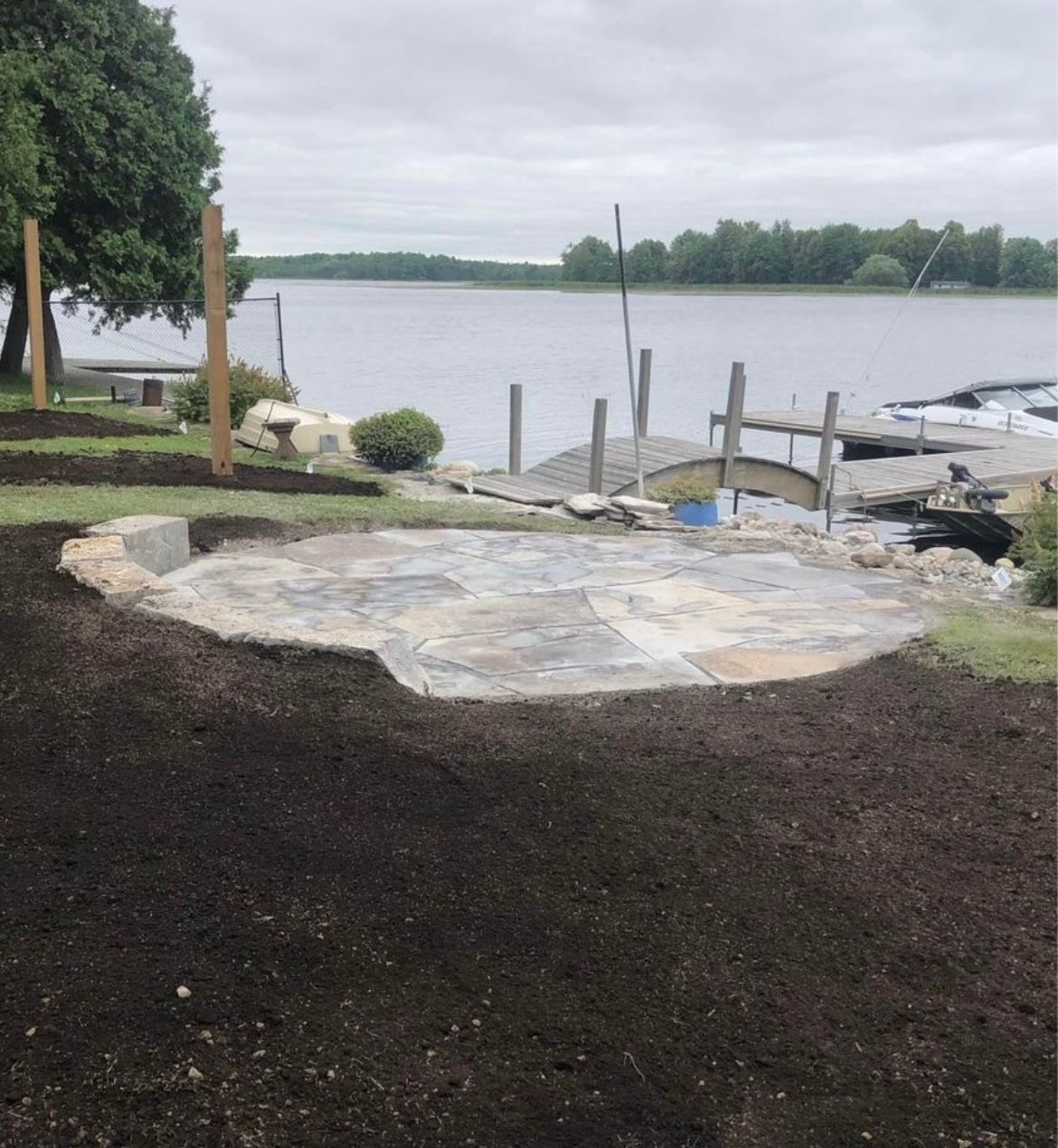 Newly constructed stone patio with lake view. Dark mulch surrounds the patio. Dock in background.
