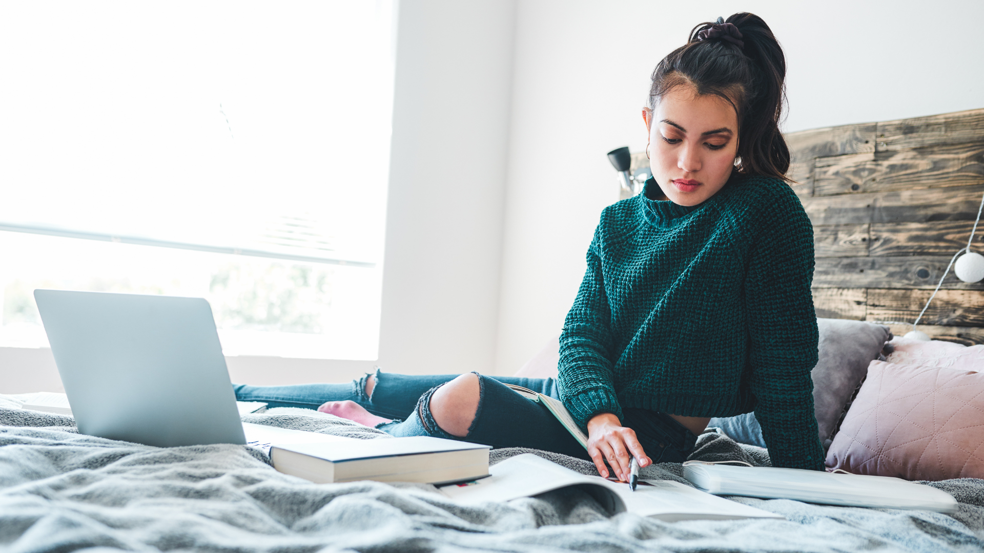 Woman studying on bed with laptop and notebook.