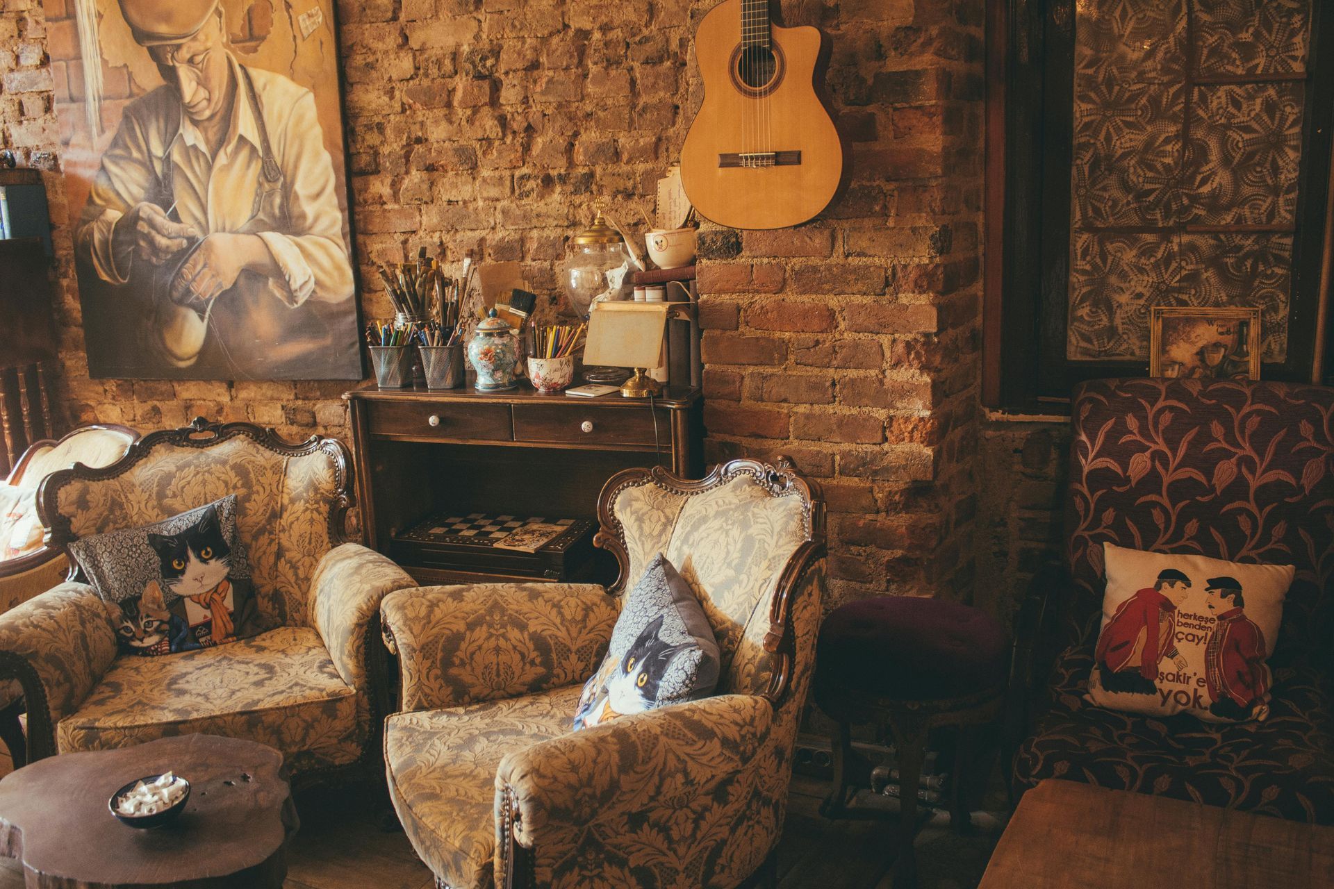 Cozy room with patterned armchairs, brick wall, artwork, a guitar, and a small table.