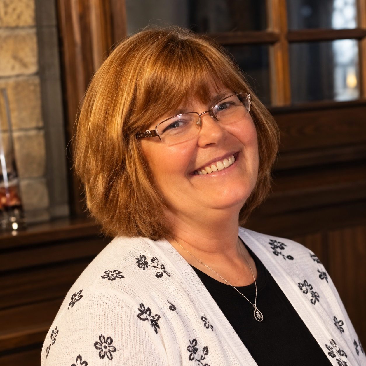 Woman with short, light brown hair and glasses, smiling, wearing a white sweater and black shirt.