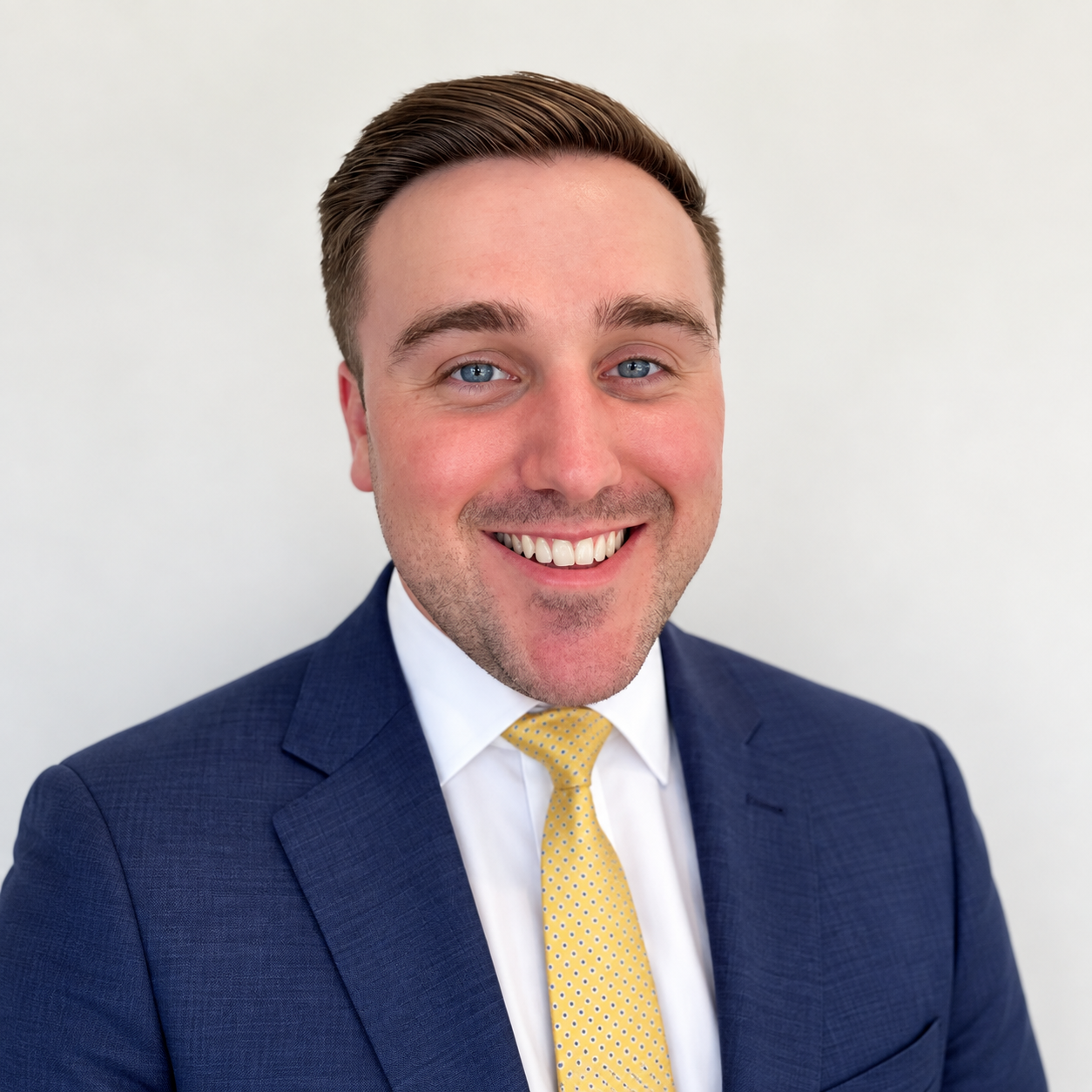 Man in navy suit, white shirt, and yellow tie smiles broadly, headshot.