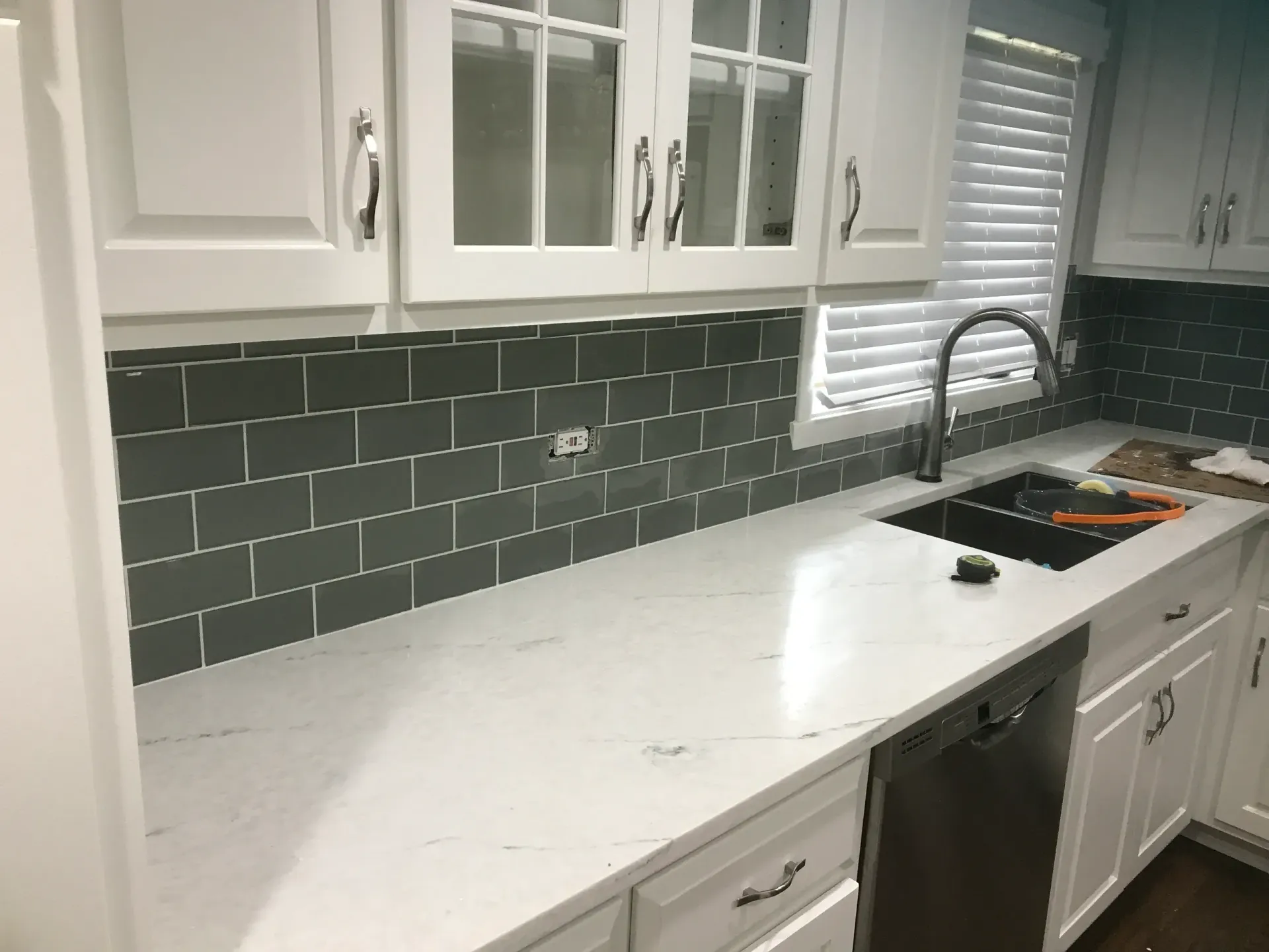 Kitchen with white cabinets, gray backsplash, and white countertops. Stainless steel appliances and a black sink.