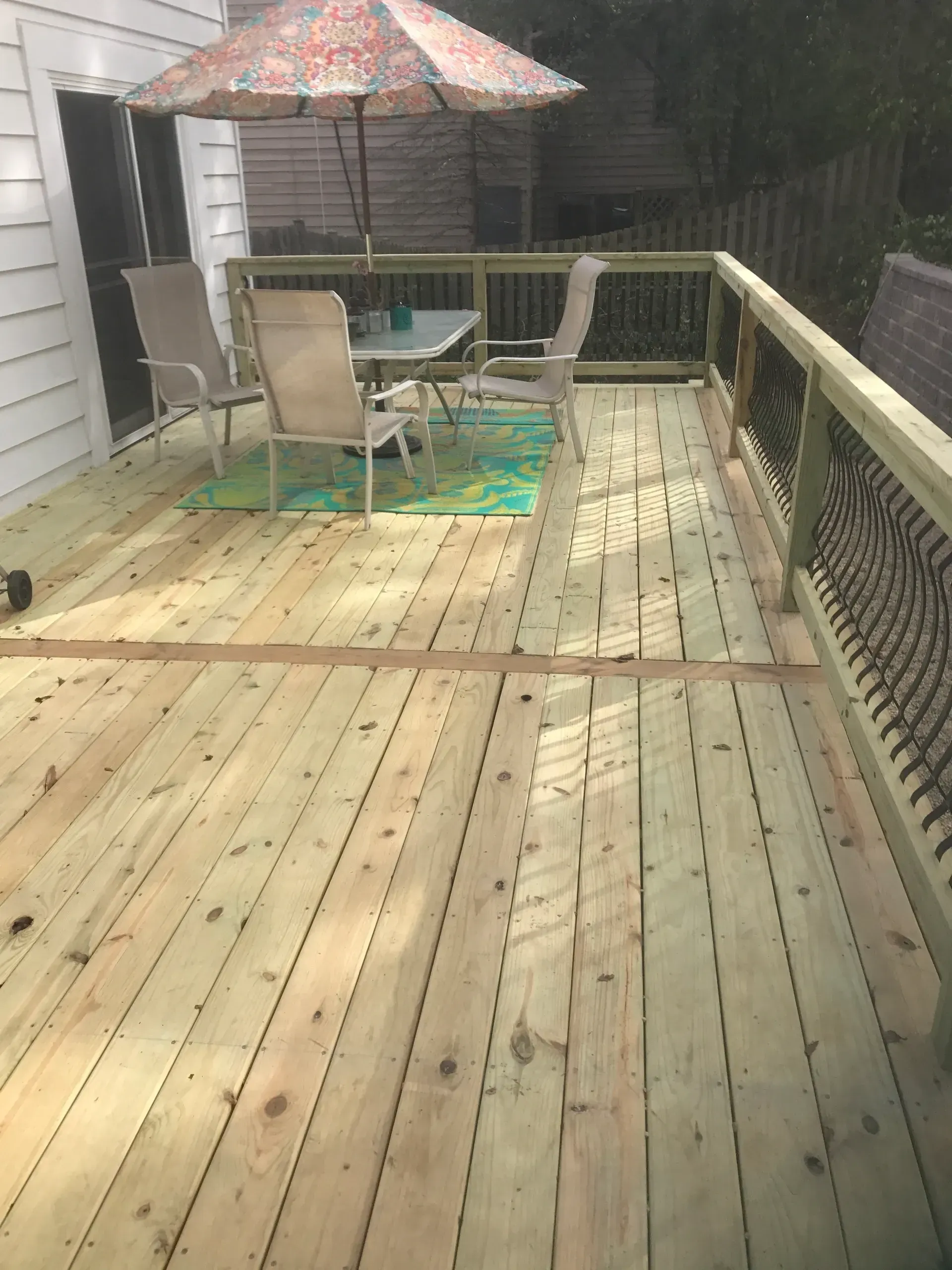 Wooden deck with patio furniture, umbrella, and metal railing.