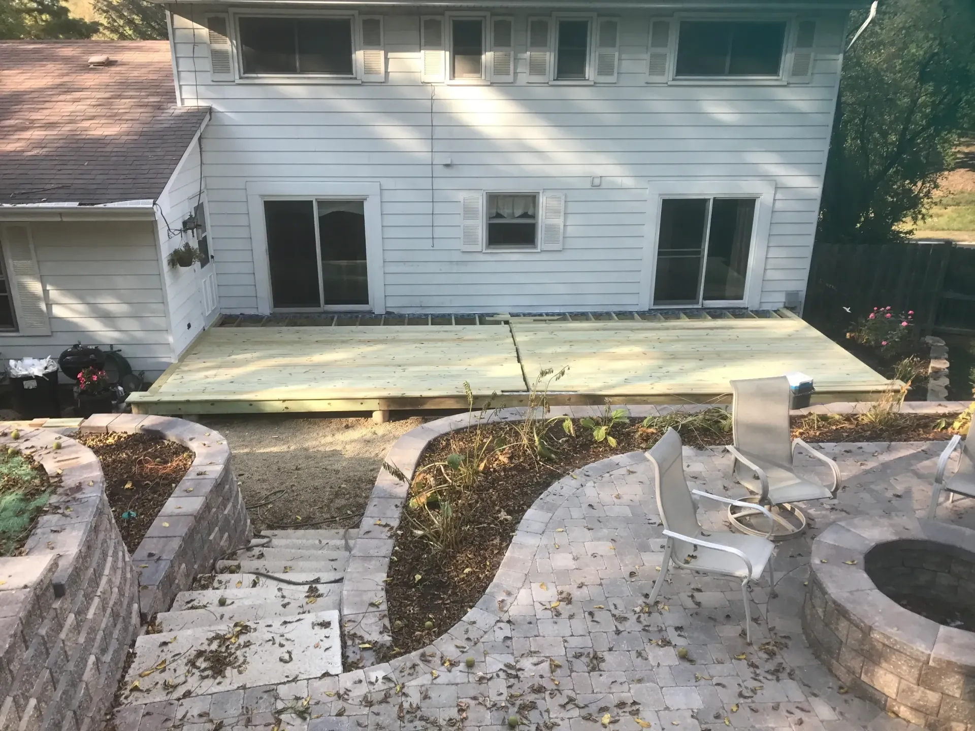 Backyard with a two-story house, deck, stone patio, retaining walls, fire pit, and lounge chairs.