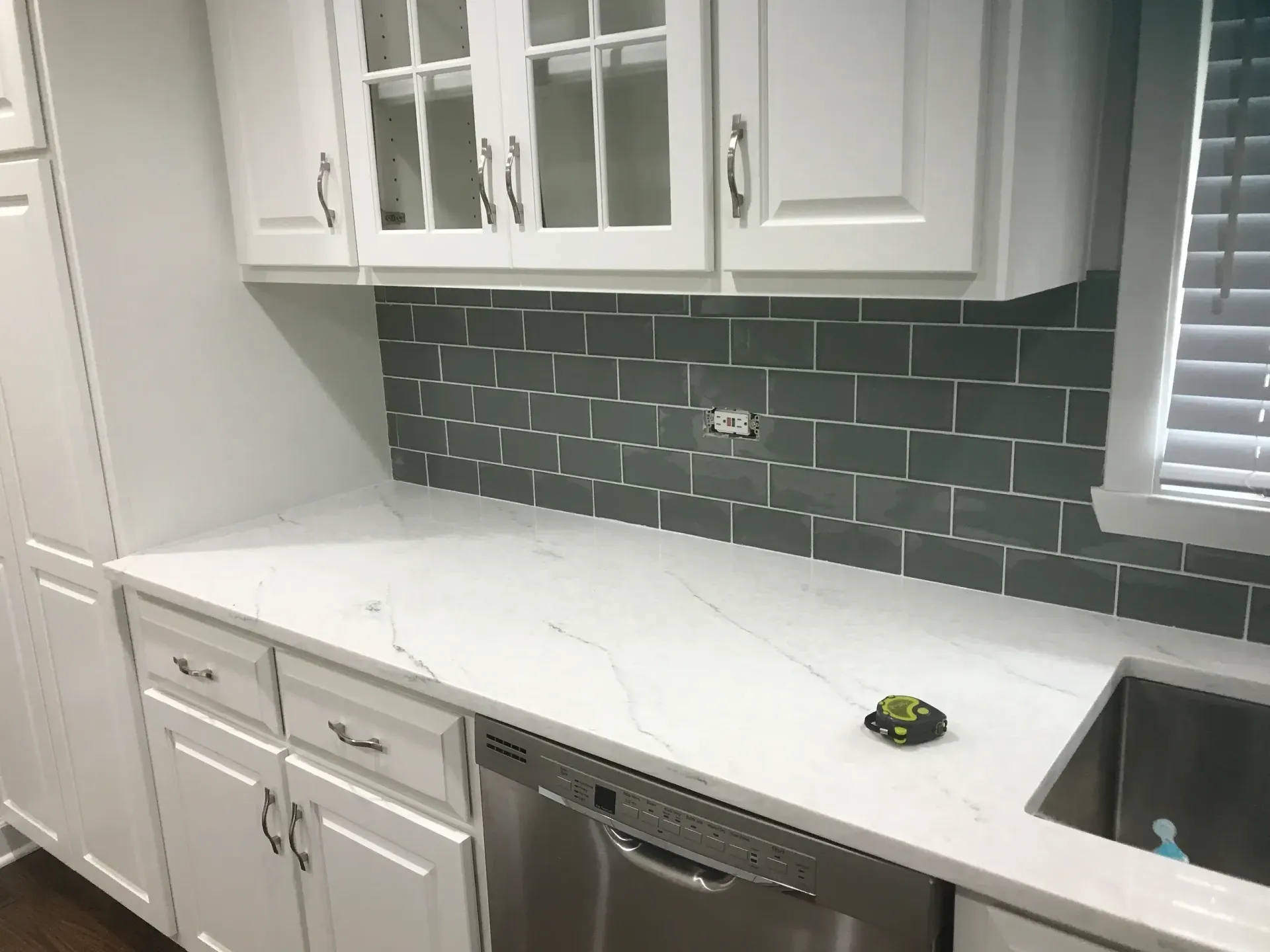 White kitchen with gray subway tile backsplash, white countertops, and stainless steel appliances.