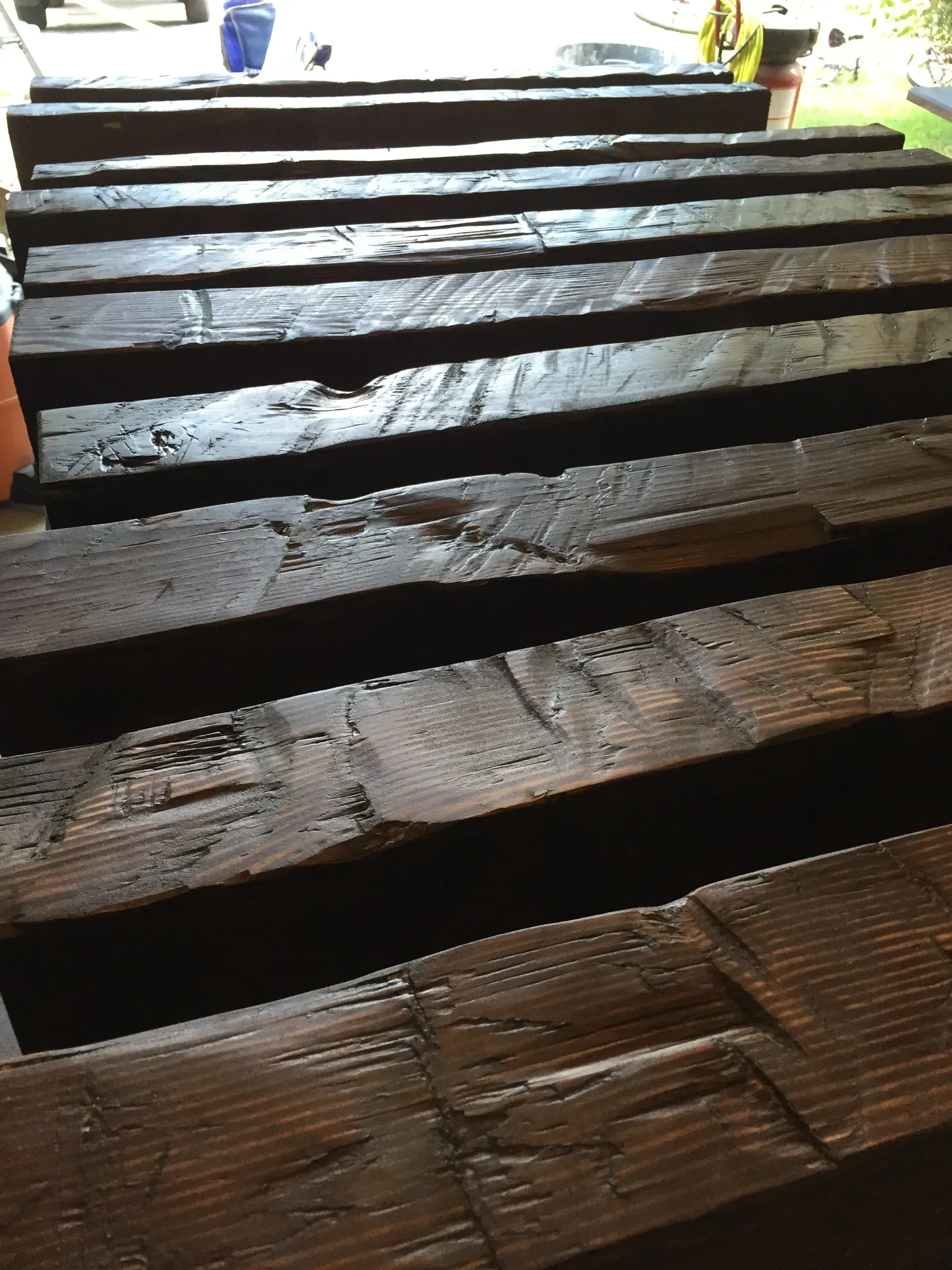 Dark stained wooden beams, stacked and arranged in a workshop setting.