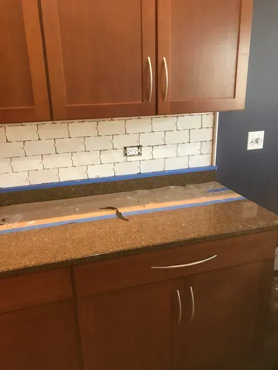 Kitchen with brown cabinets and countertop, white subway tile backsplash, blue tape, and outlet.