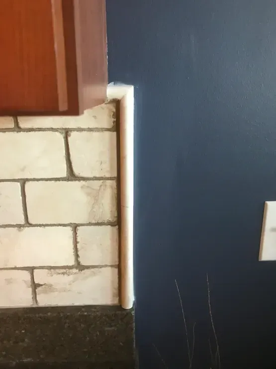 White-tiled backsplash, dark blue wall, and brown cabinet meeting with white molding; an electrical outlet is visible.