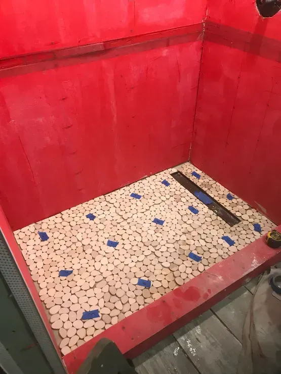 Shower stall with wooden tile floor, red walls, and linear drain.