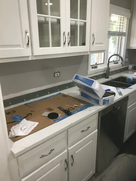 Kitchen renovation in progress: white cabinets, gray backsplash, countertop work area, sink, and faucet.