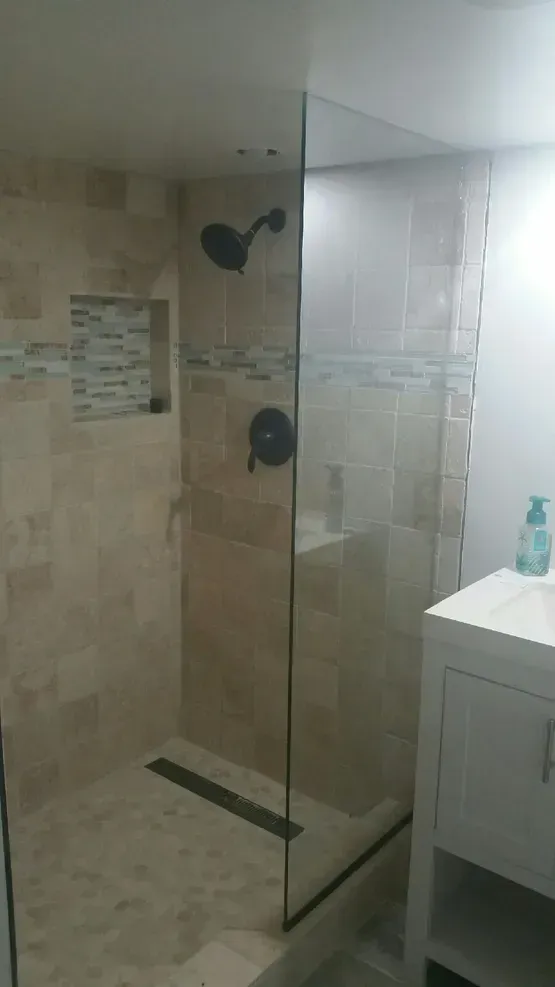 Shower with glass door, dark fixtures, beige tile, and vanity on the right.