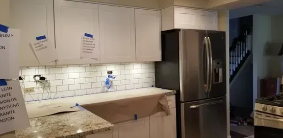 Kitchen undergoing renovation with white cabinets, stainless steel refrigerator, and subway tile backsplash.