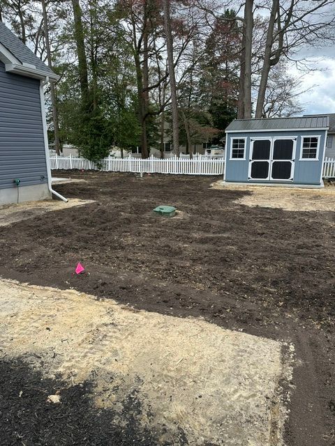 Bare yard with dirt and gravel, white fence, blue house on left, and a small shed in the back.