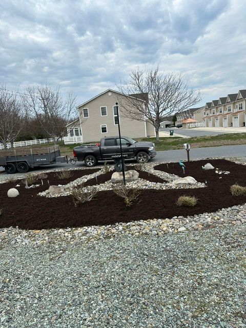 Mulched rock garden with small trees and white stones beside a parked black car and apartment building