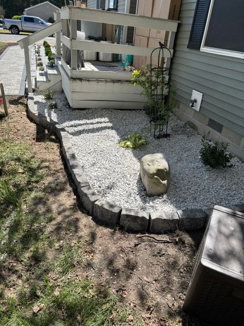 Small gravel garden beside a house with a white bench swing and stepping stones bordered by dark rocks