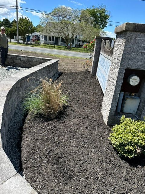 Landscaped walkway with stone walls, mulch, shrubs, and a sign at an outdoor entrance.