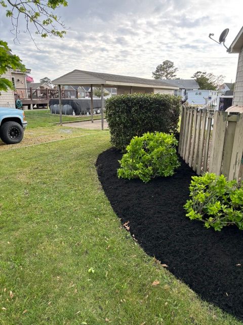 Backyard with curved black mulch bed, green shrubs, wooden fence, and a house in the background