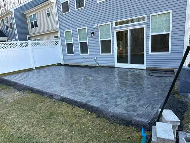 Stamped concrete patio beside blue house with sliding glass doors and white fence