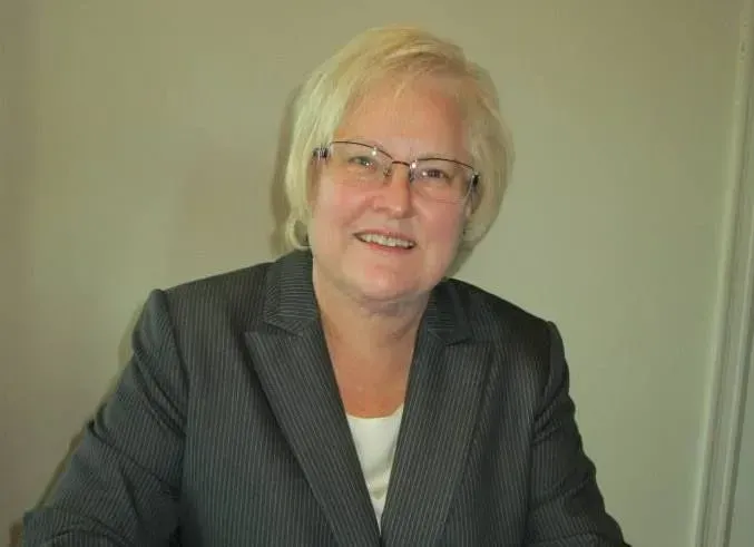 A woman in a suit and glasses is smiling for the camera.